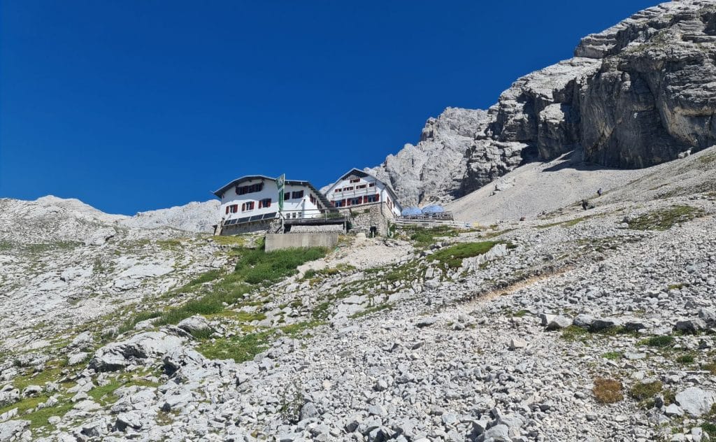 På bilden visas Knorrhütte, en vit bergsstuga byggd på en brant, stenig sluttning.