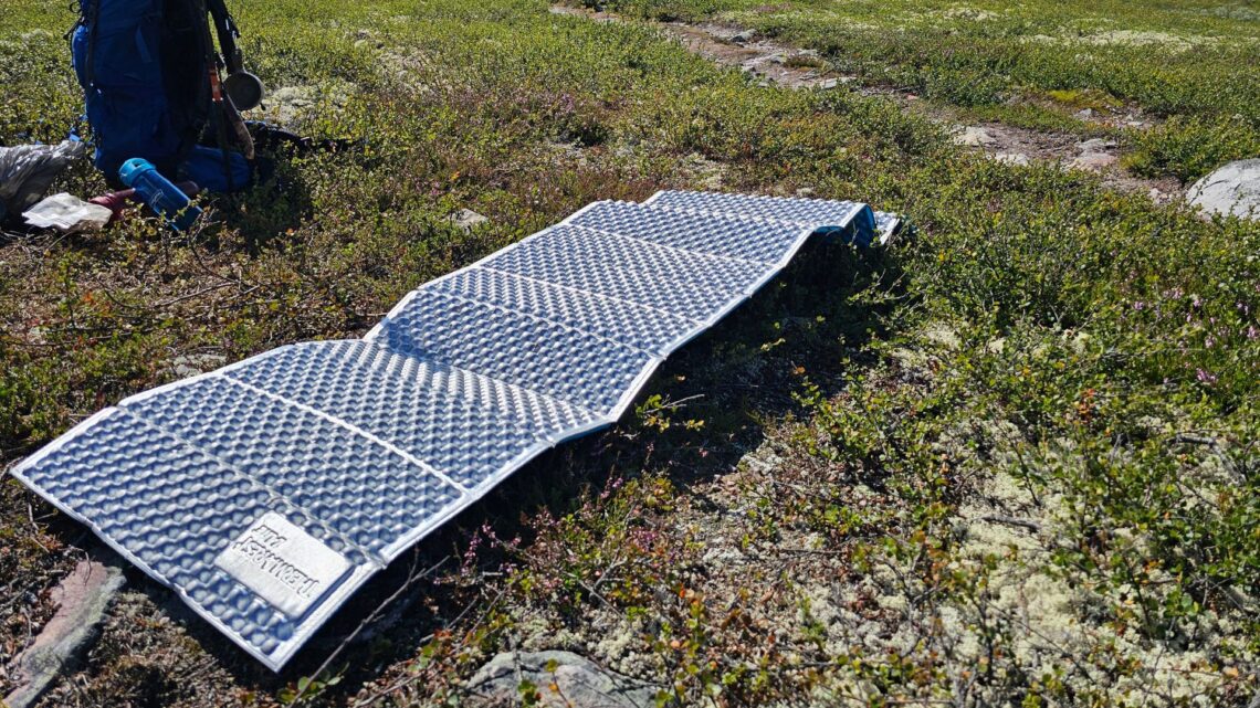 Silverfärgat liggunderlag i cellplast ligger på marken bredvid en ryggsäck