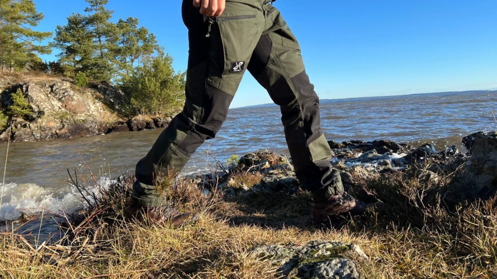 En person bär ett par Nordwand Pro Pants vid Vänerns strand.
