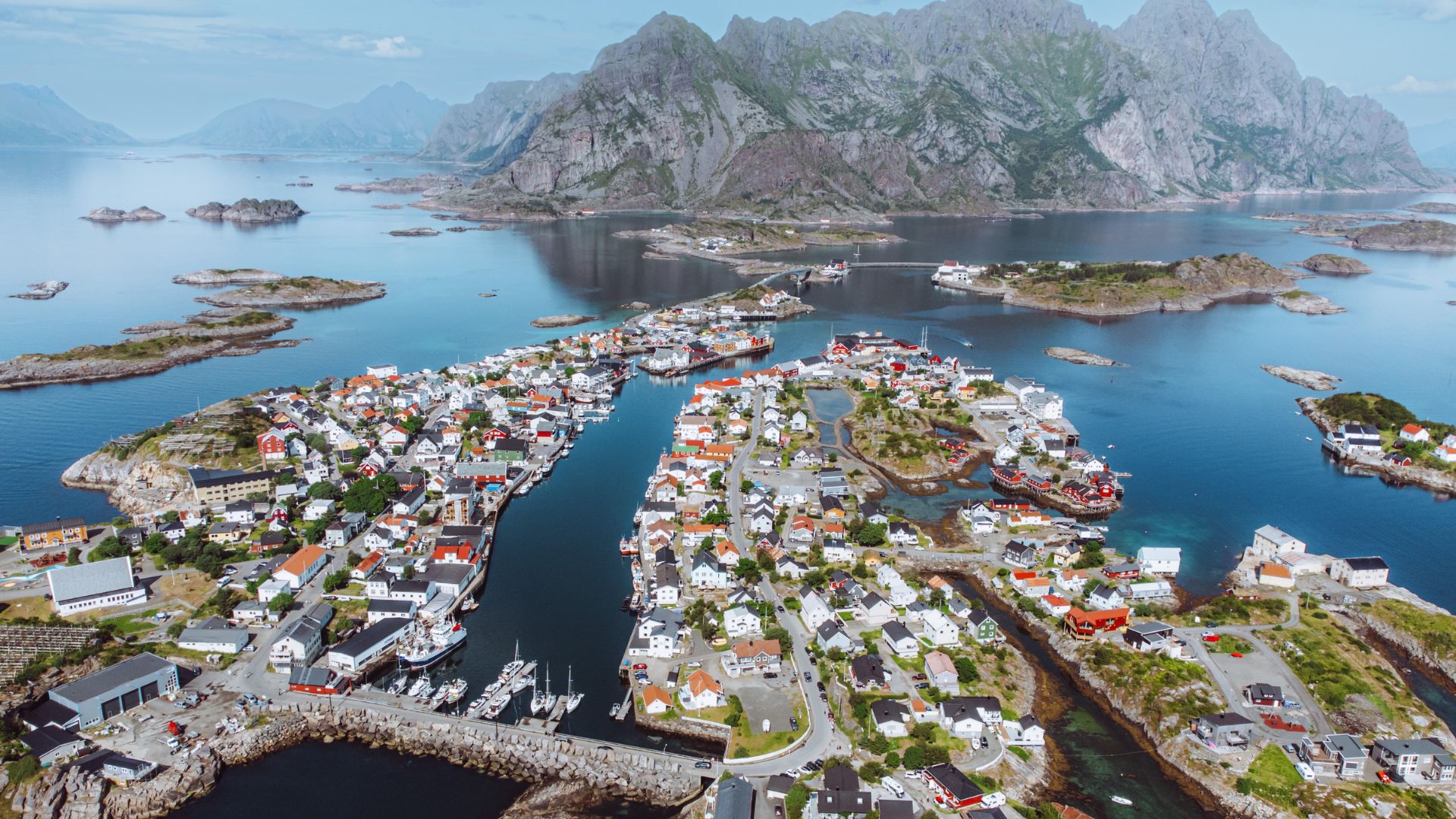 Henningsvaer sett från ovan. Små trähus täcker de sammanbundna öarna och i bakgrunden syns berg.