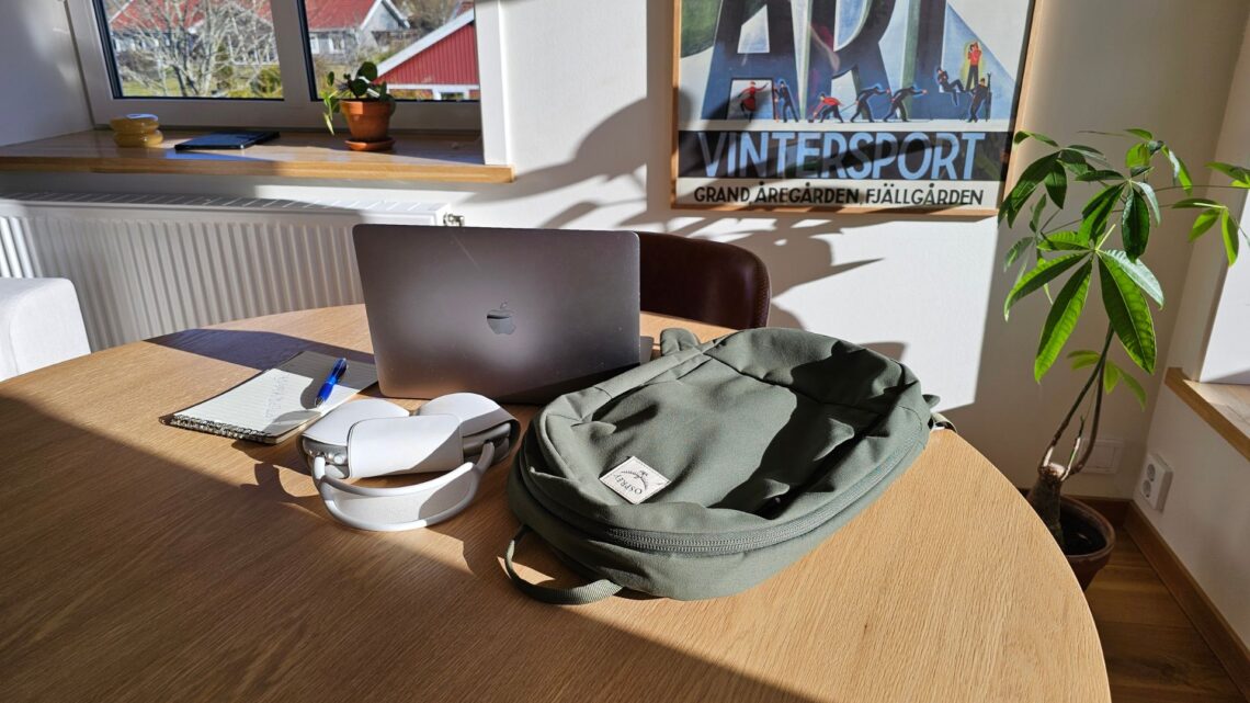 Osprey Arcane Small ryggsäck placerad på ett bord bredvid en laptop och ett anteckningsblock.