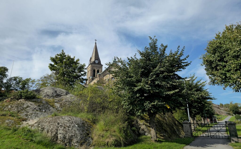 Tornet på Fjällbacka kyrka sticker upp bakom gröna buskar och träd.