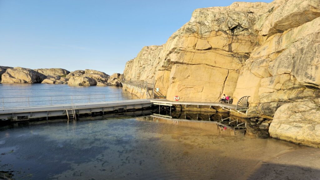 Valleviksbadet vid Smögen, bryggan kantar klippväggen och en liten strand visas närmast i bild.