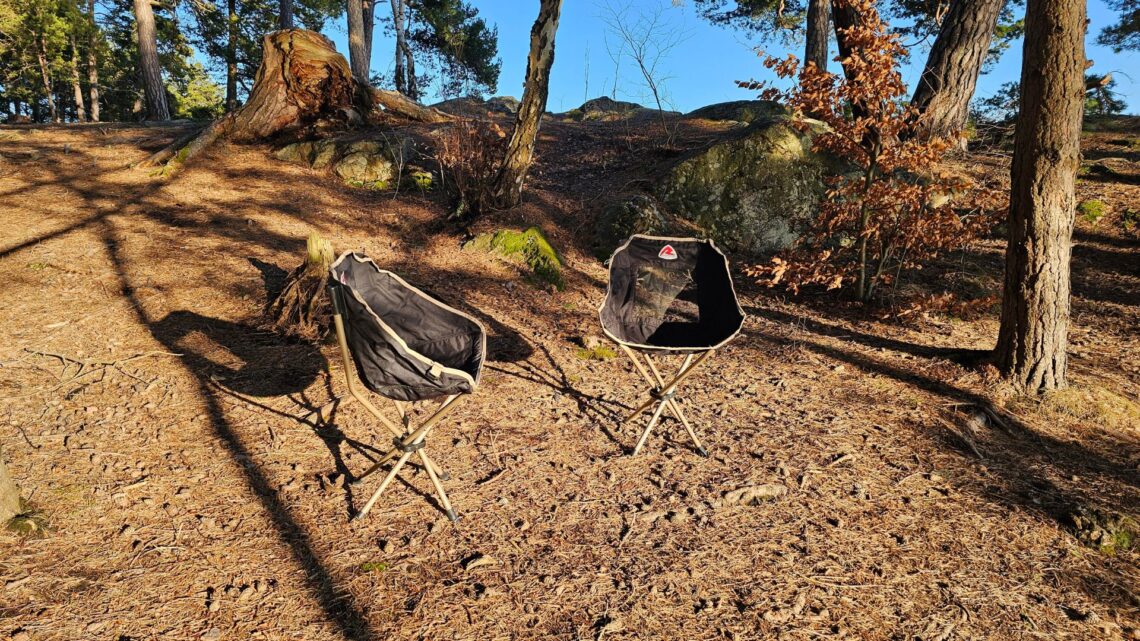 Två hopfällbara campingstolar i en skogsglänta omgivna av tallar.