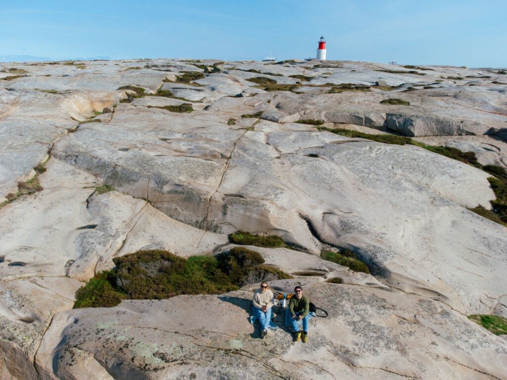 Ett par sitter på klipporna med Hållö Fyr i bakgrunden.