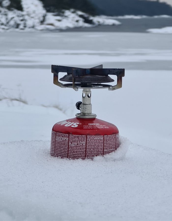 Stormköket primus mimer testas i snön i bakgrunden syn klippor skog och en frusen sjö