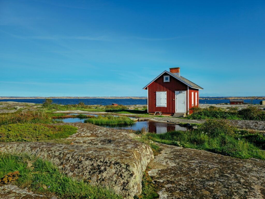 Röd stuga står i stenigt landskap med kortvuxen grönska runt om.